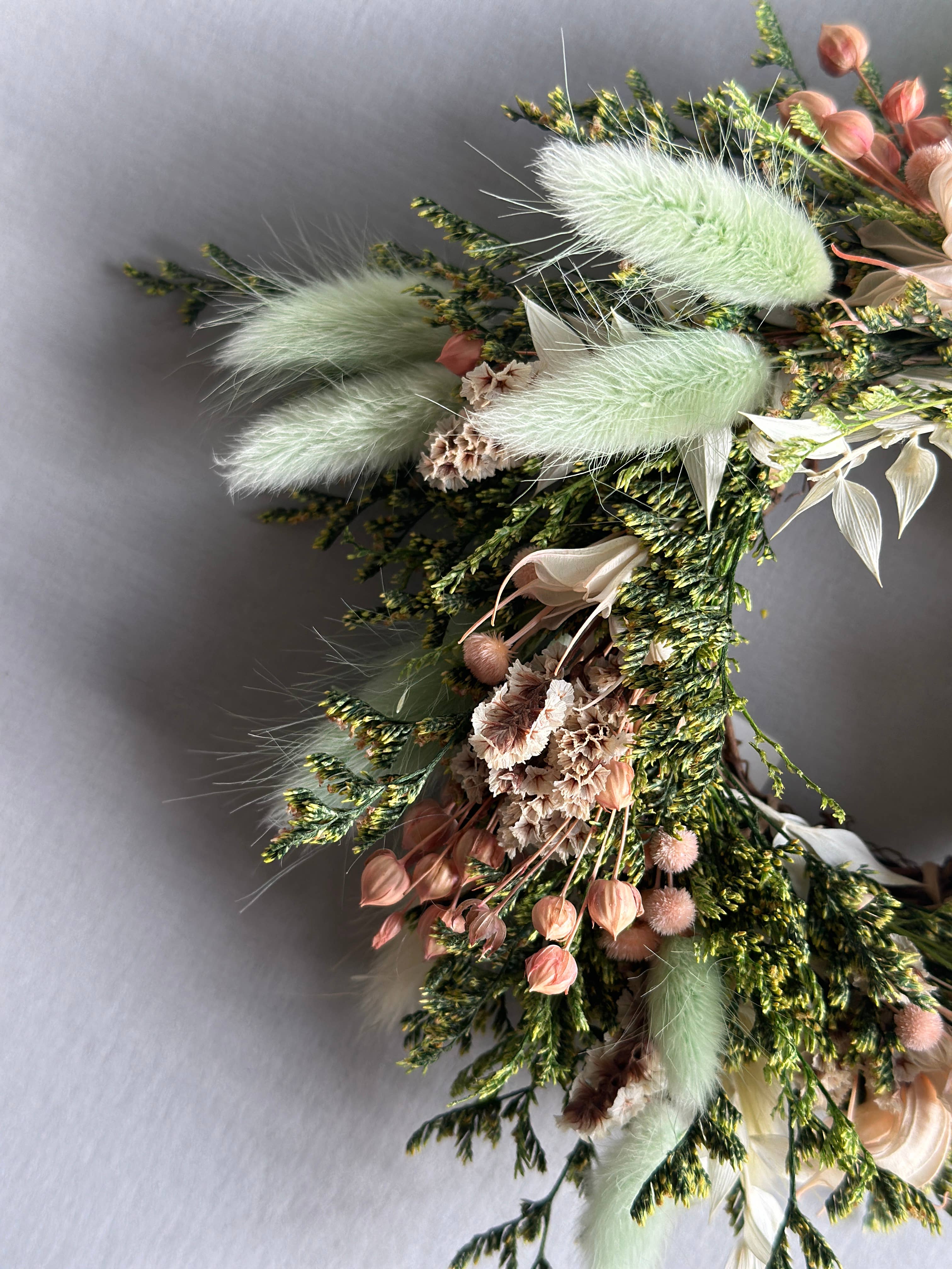 Close-up of a floral arrangement with greenery and dried flowers on a light gray background