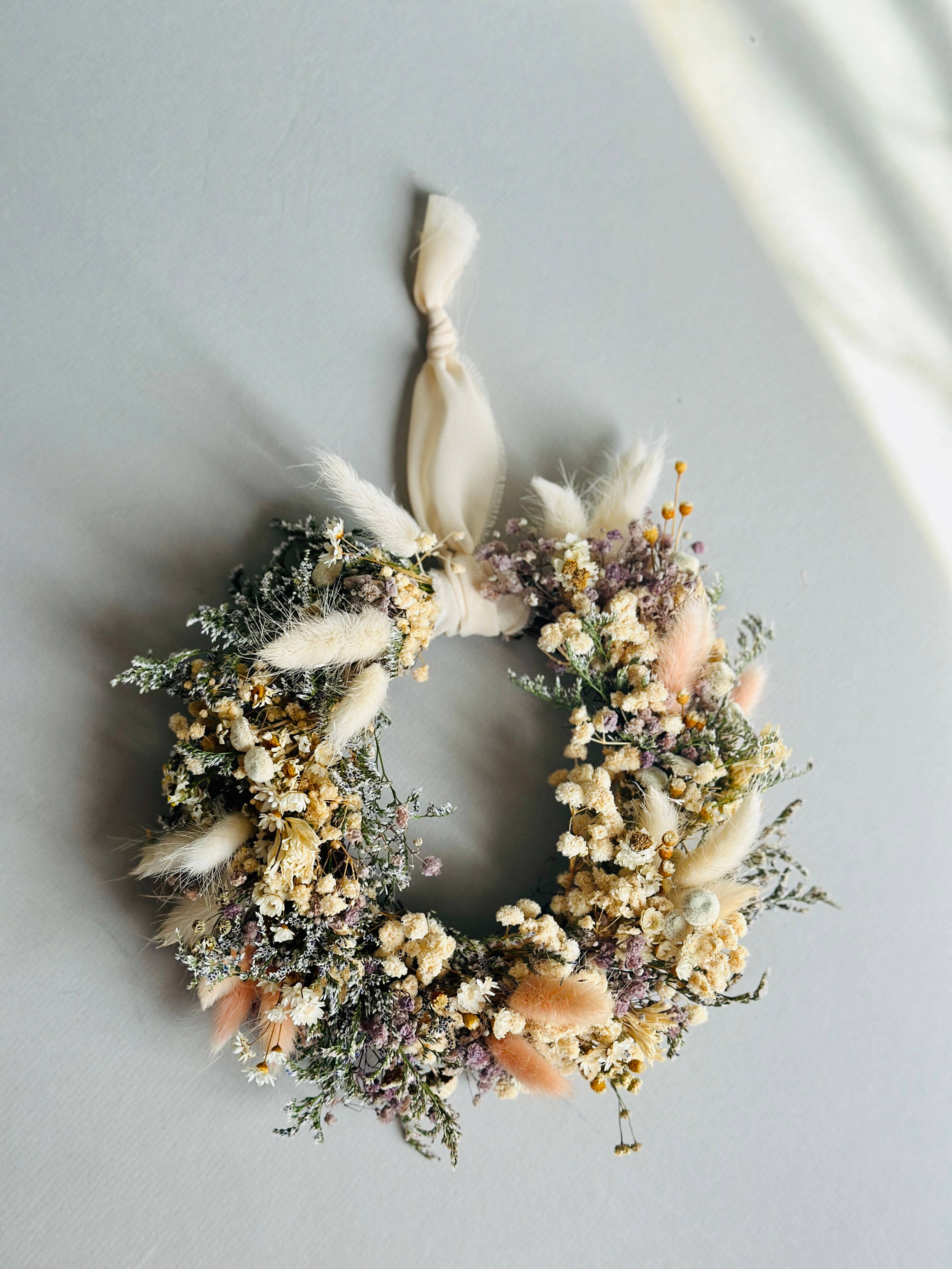 Decorative wreath with dried flowers and a ribbon on a light gray background
